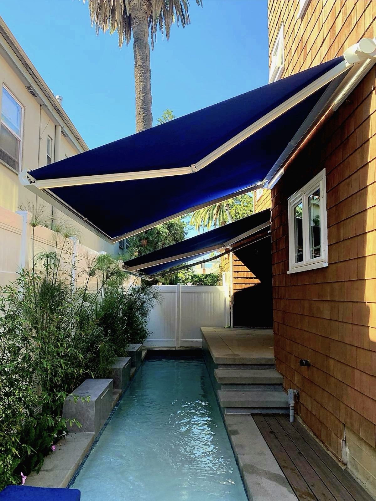 Twin blue cassette retractable awnings extended over a lap pool