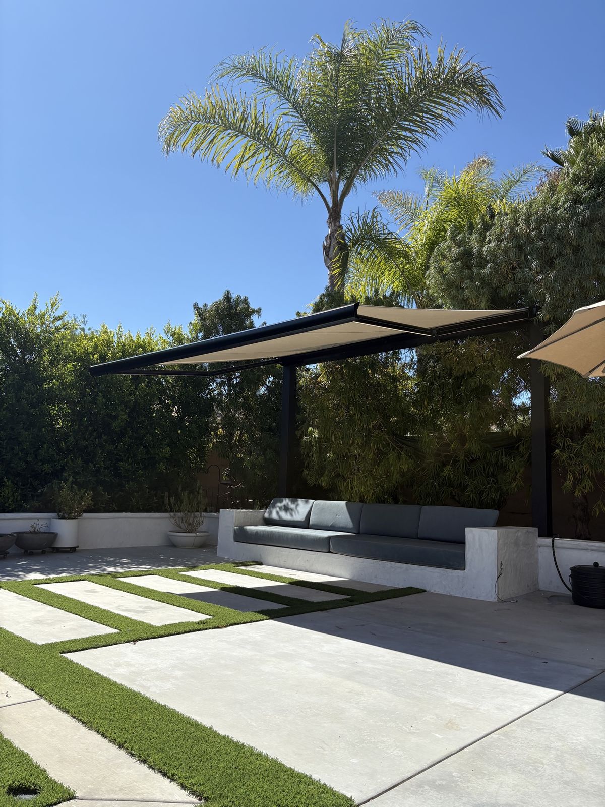 Freestanding retractable awning with black frame over a built-in outdoor lounge sofa