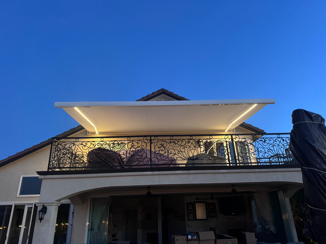 Retractable awning with LED lighting glowing against a deep-blue dusk sky over a wrought-iron balcony