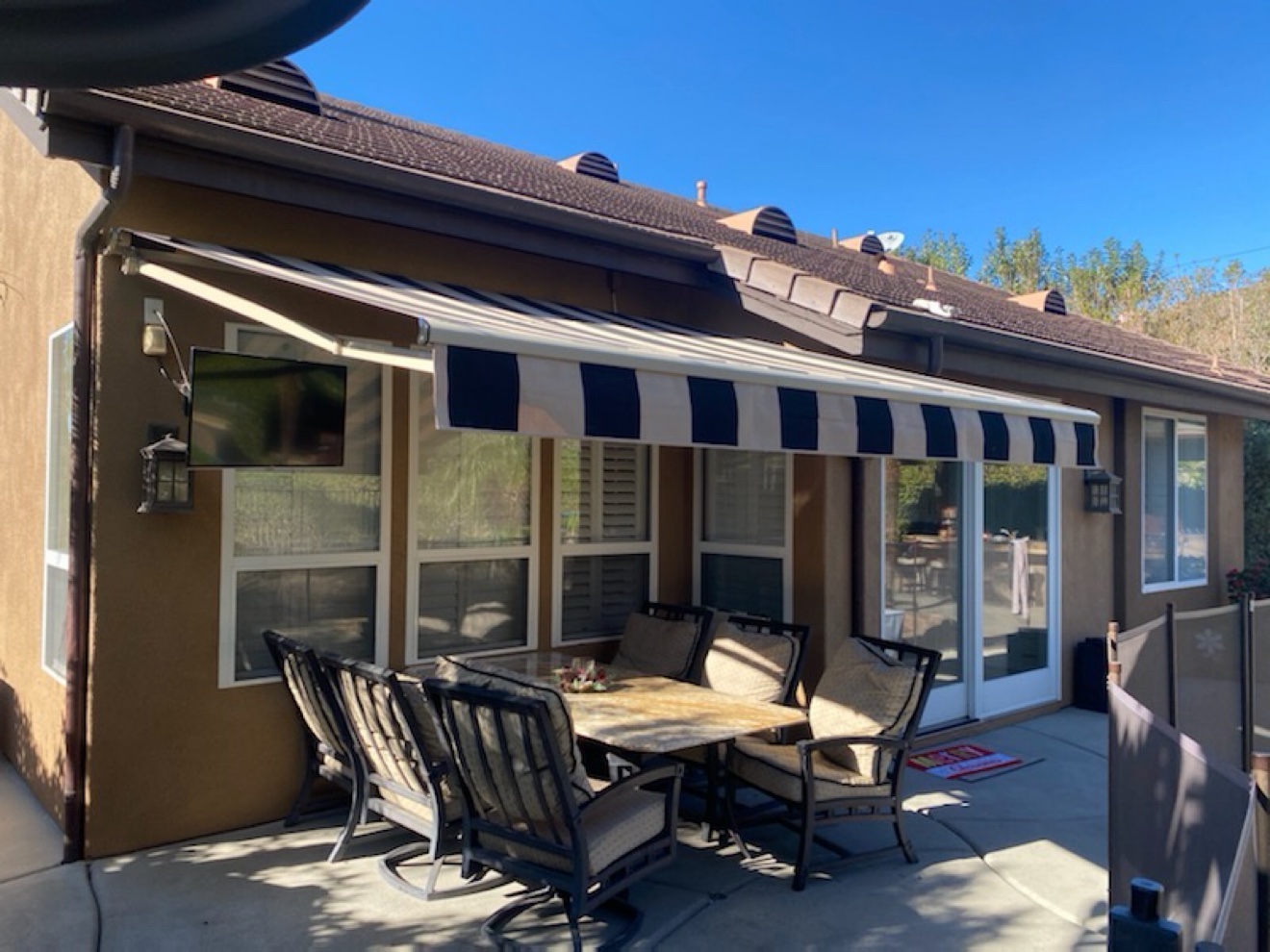 Black-and-white striped retractable awning shading a patio dining set against a stucco home