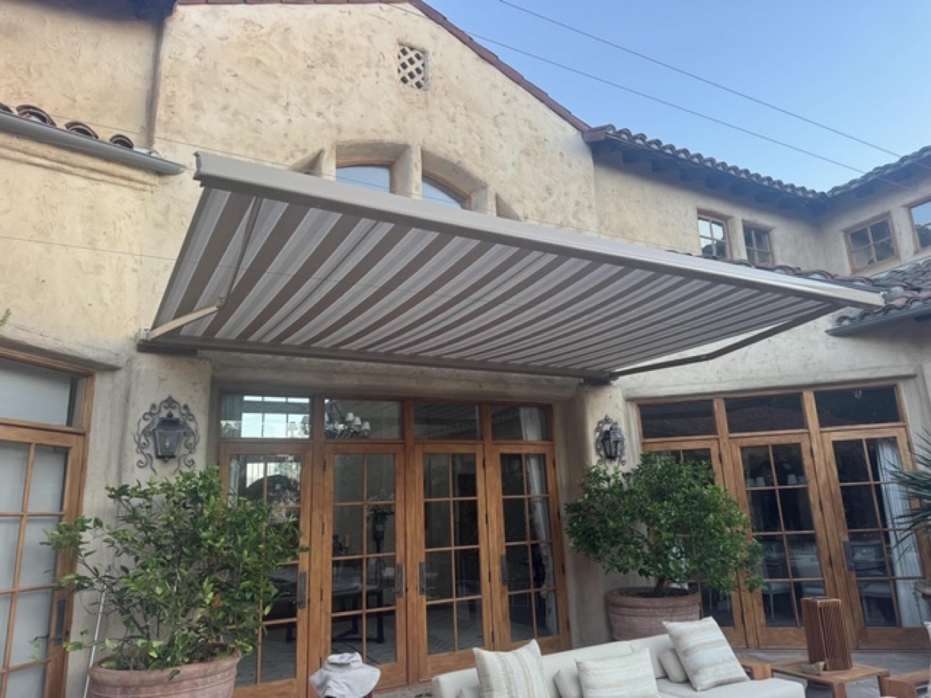 Striped retractable awning over French doors of a Spanish-style home