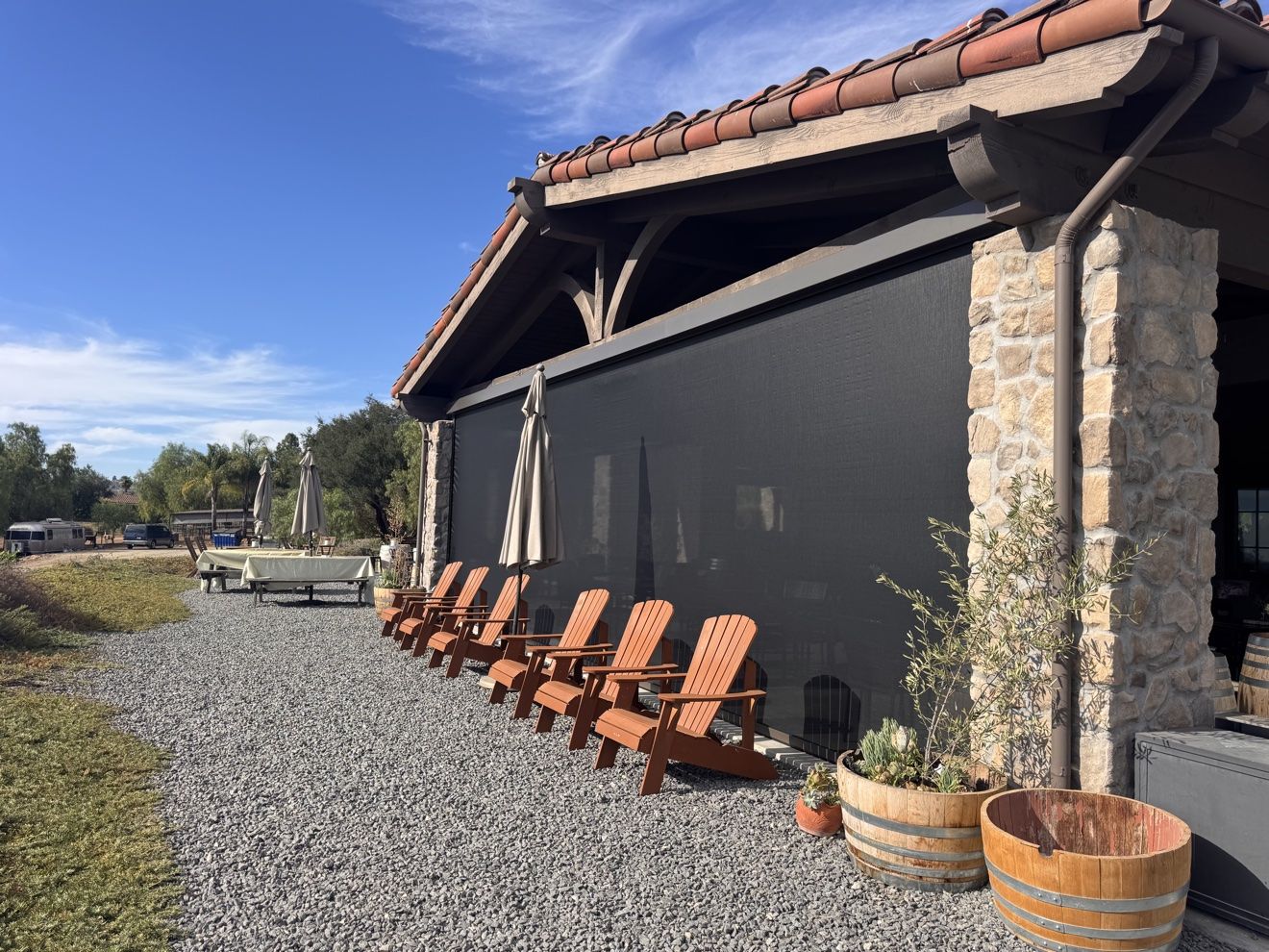 Wide view of a stone winery patio with black motorized screens fully deployed and Adirondack chairs