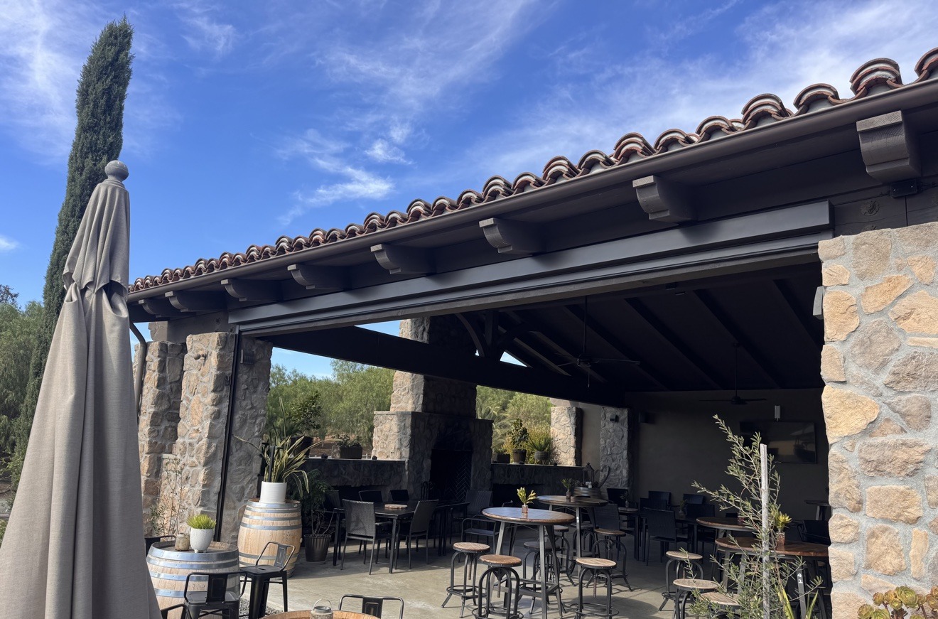 Winery patio with motorized screens fully retracted, open-air seating under a tile roof