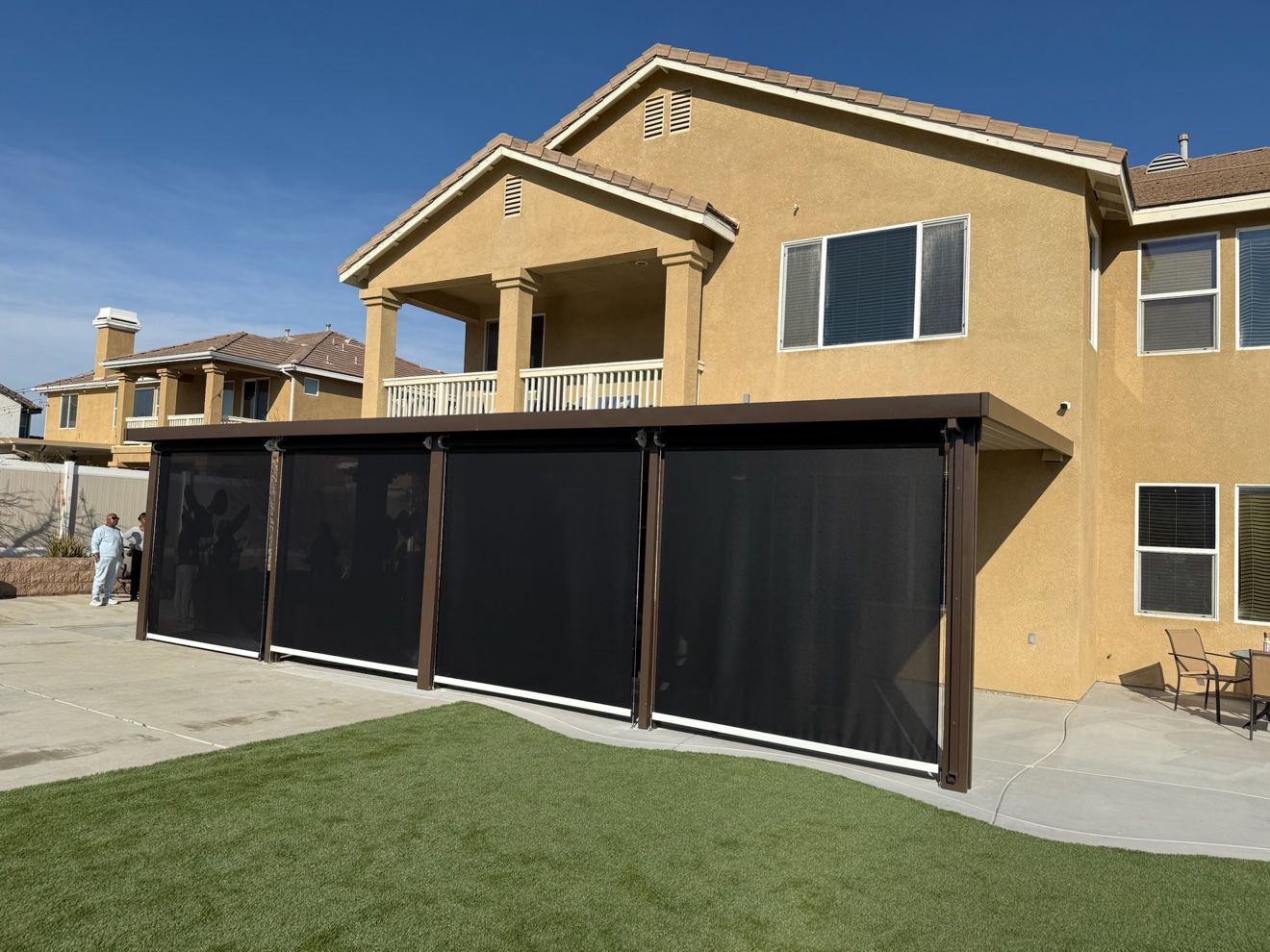 Four black motorized patio screens fully lowered under a patio cover