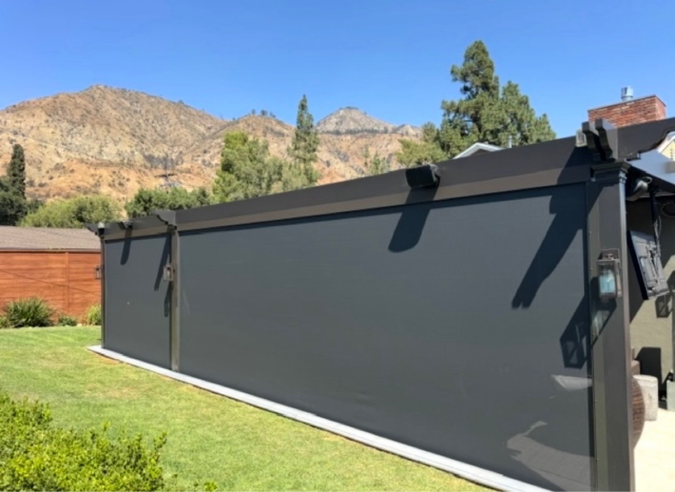 Dark motorized power screens fully deployed on a backyard pergola with mountain views behind