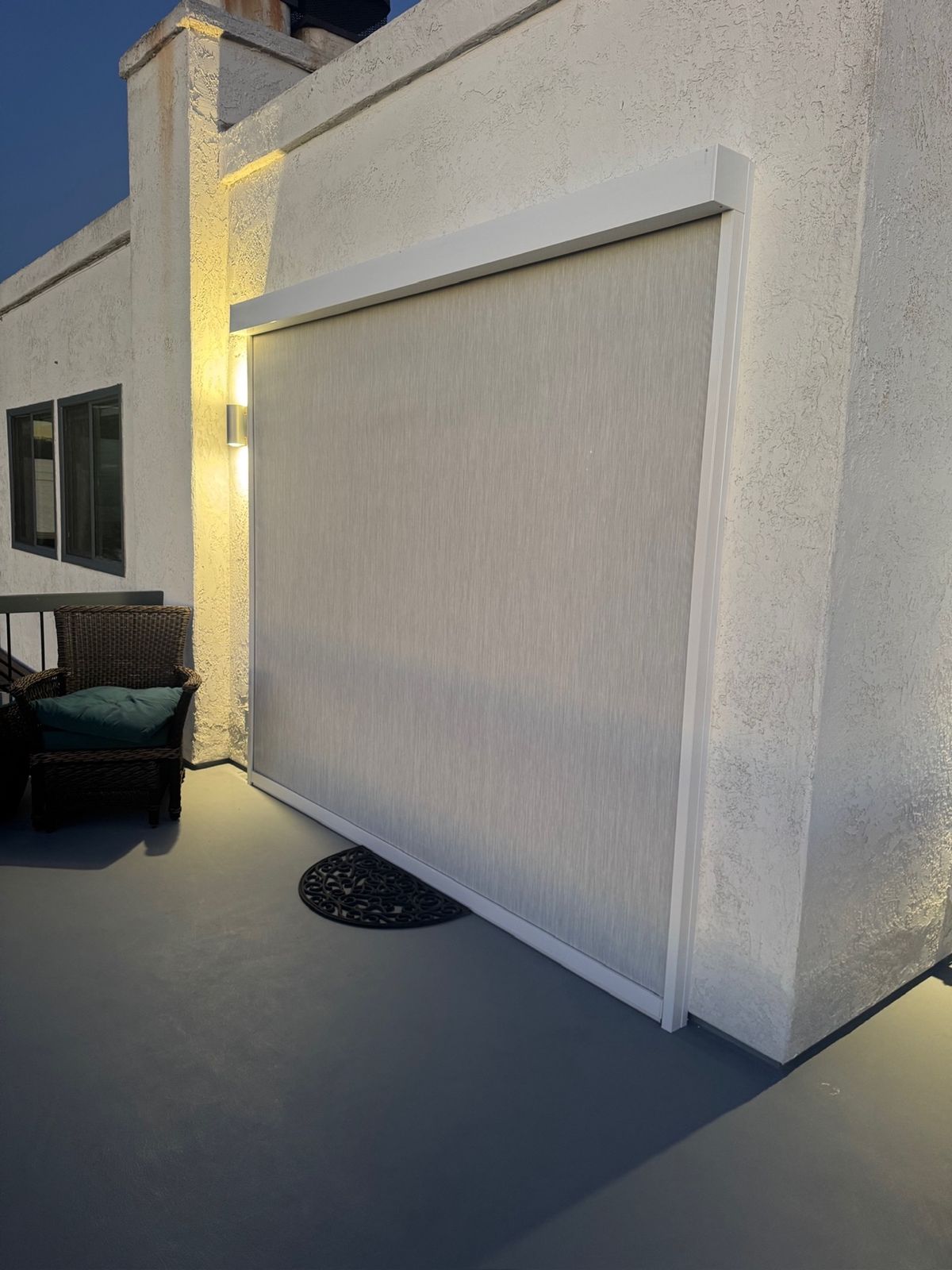 White-cassette motorized patio screen lowered on a balcony patio at dusk